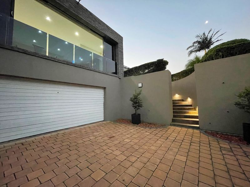 Modern exterior view featuring a paved driveway, integrated garage, and illuminated stone staircase leading to the upper level.