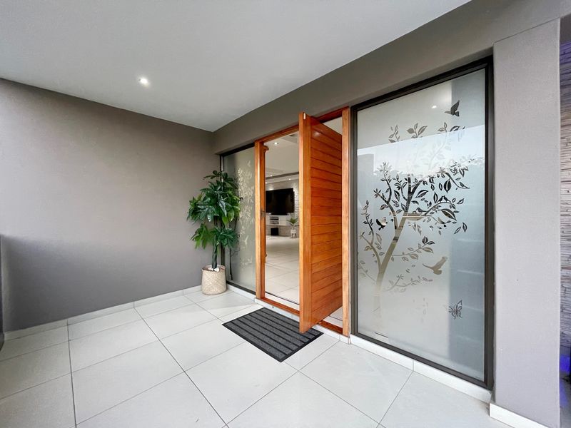Modern entrance featuring a large timber pivot door and decorative frosted glass sidelights, leading into a bright, tiled interior space.