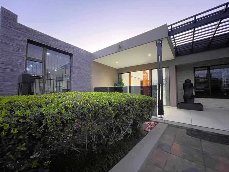 Modern front entrance featuring stone cladding, a covered patio with glass balustrades, and a well-maintained garden area.