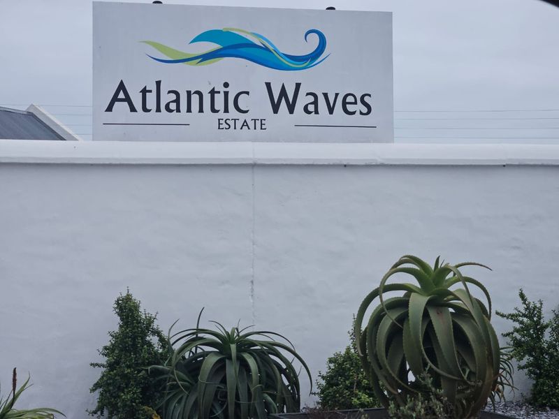Entrance signage for the Atlantic Waves Estate, featuring a clean white boundary wall and landscaped garden elements.