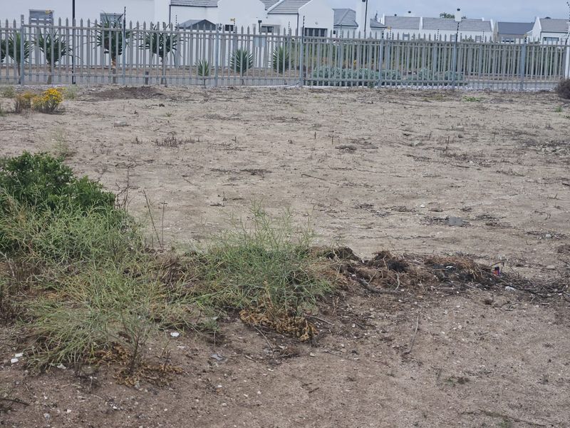 An undeveloped garden area featuring sandy ground and secure metal perimeter fencing with integrated electric security wires.