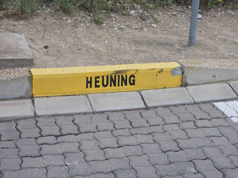 A close-up view of a painted yellow concrete kerb with signage, bordering a paved driveway area.