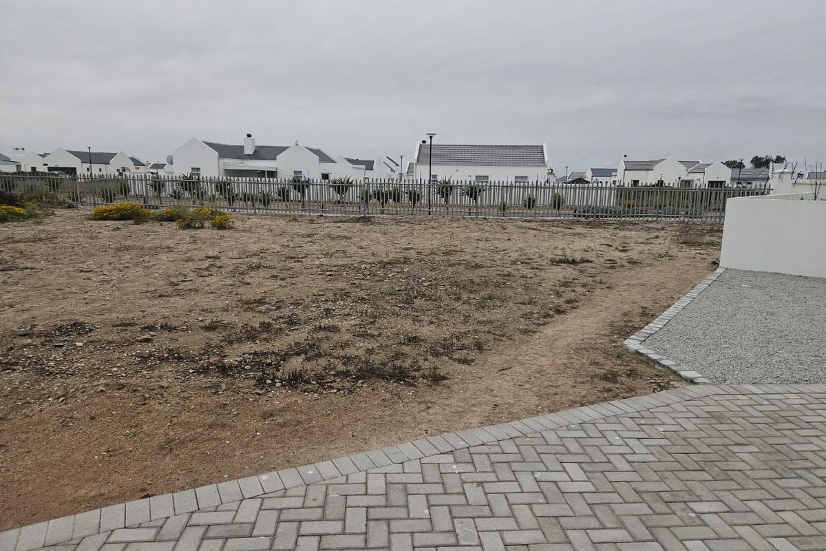 An undeveloped garden area featuring paved walkways, gravel borders, and metal perimeter fencing, offering a blank canvas for landscaping.