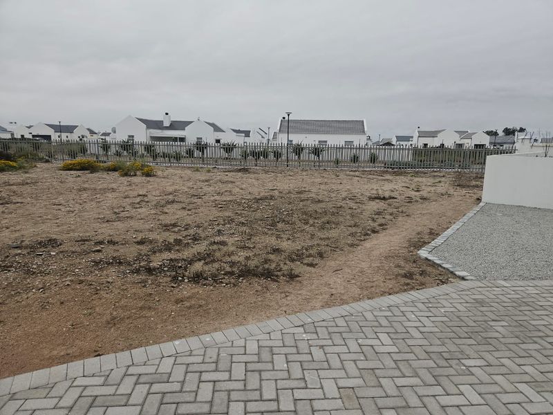 An undeveloped garden area featuring paved walkways, gravel borders, and metal perimeter fencing, offering a blank canvas for landscaping.
