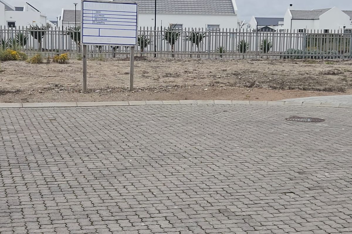 A street-level view of a paved driveway area featuring metal security fencing and a construction information sign in a residential estate setting.