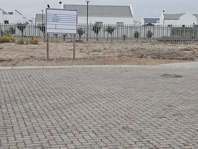 A street-level view of a paved driveway area featuring metal security fencing and a construction information sign in a residential estate setting.