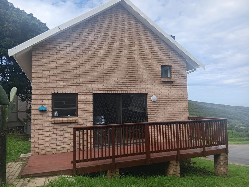 Rear view of the cottage featuring a brick facade, a raised timber deck with balustrade, and sliding glass doors with security gates.