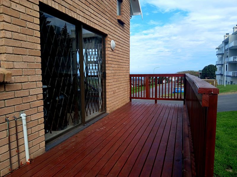 An elevated timber balcony featuring a wooden balustrade, brick exterior wall, and sliding glass door access with a security gate.
