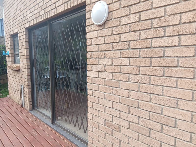 A view of the exterior brick facade featuring a sliding glass door with a security gate and wooden decking.