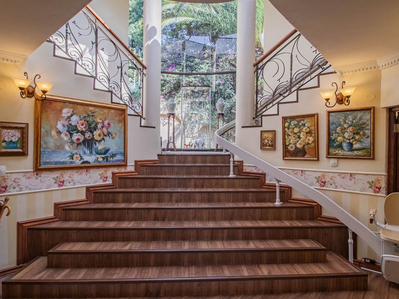 Grand entrance foyer featuring a wide wooden staircase with ornate wrought iron railings, decorative columns, and a built-in stairlift leading to an upper level.