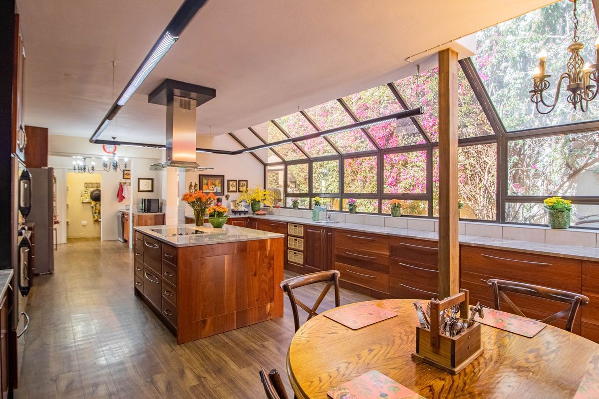 Spacious kitchen featuring warm wood cabinetry, a central island with stone countertops, and a unique glass conservatory-style roof providing abundant natural light.