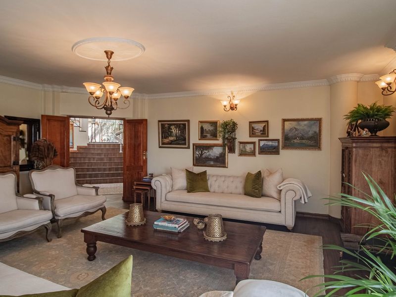 A spacious and elegant living room featuring classic crown molding, a decorative ceiling rose, and warm hardwood flooring with access to an adjacent staircase.