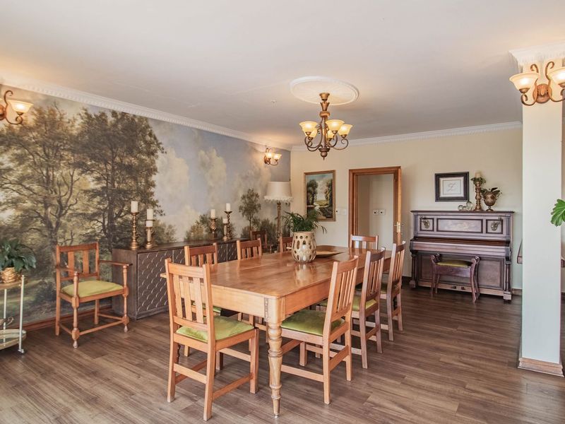 Spacious dining room featuring wood-look laminate flooring, decorative crown molding, a central ceiling rose, and a large-scale landscape wall mural.