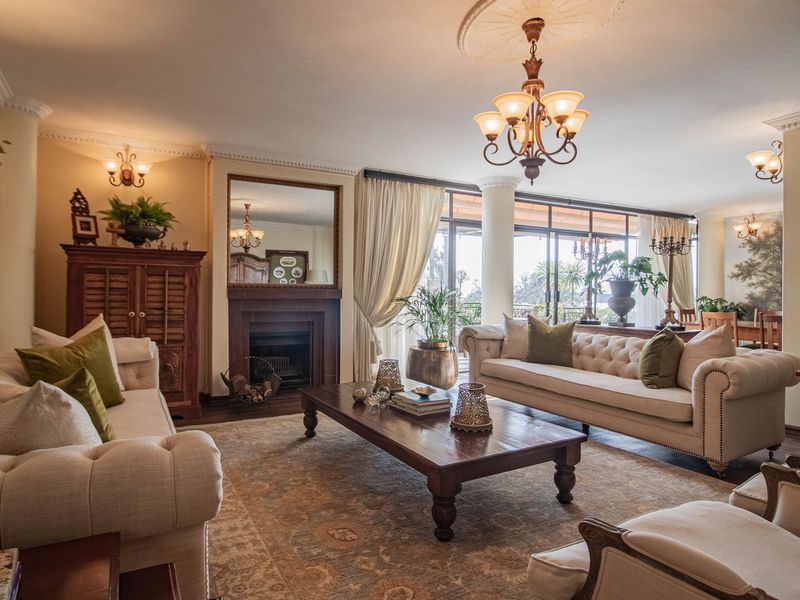 Spacious living room featuring a fireplace, elegant crown molding, ceiling roses, chandeliers, and large sliding glass doors leading to an outdoor area.