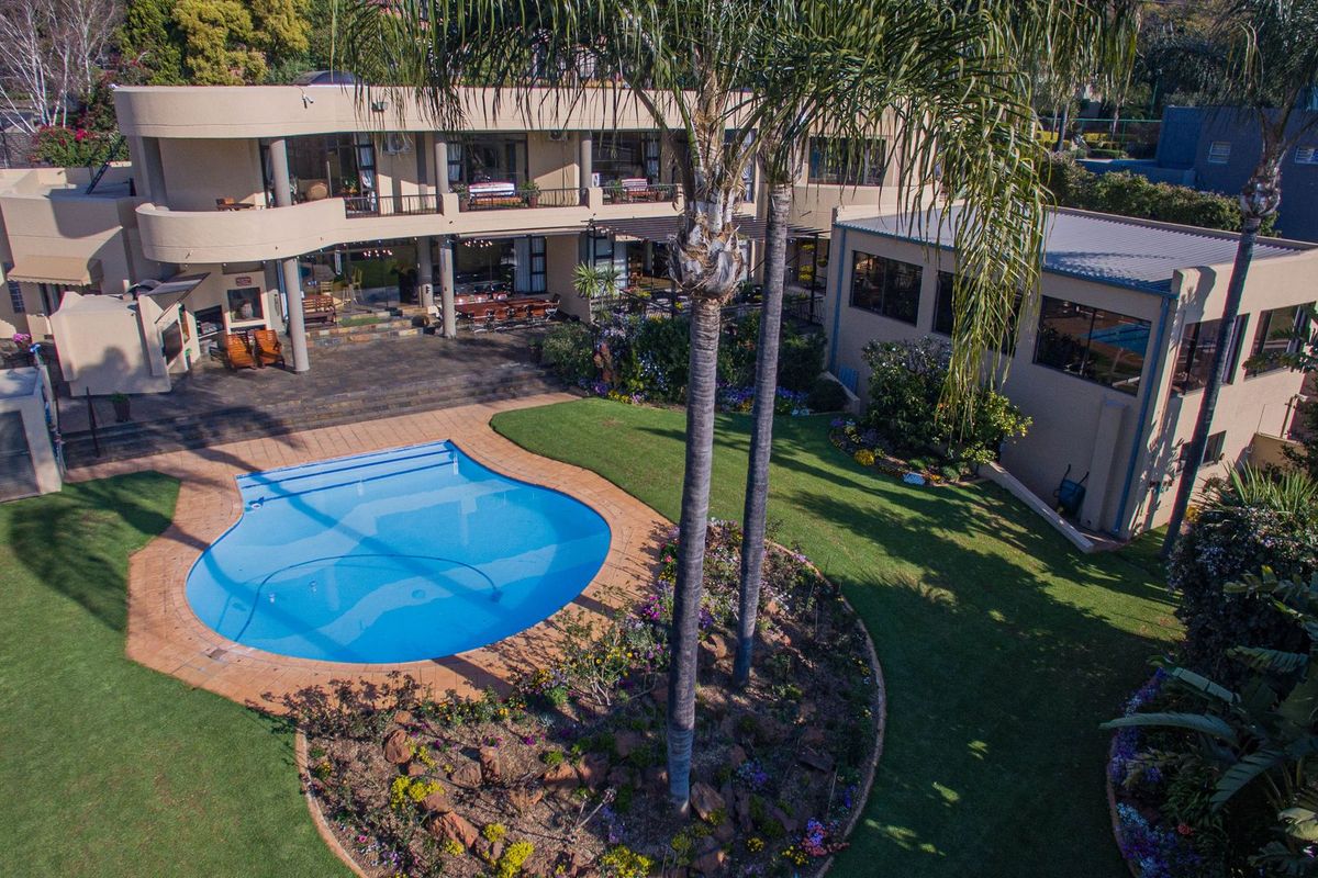 Aerial view of a spacious property featuring a large swimming pool, manicured garden, paved patio area, and a multi-level residence with balconies.