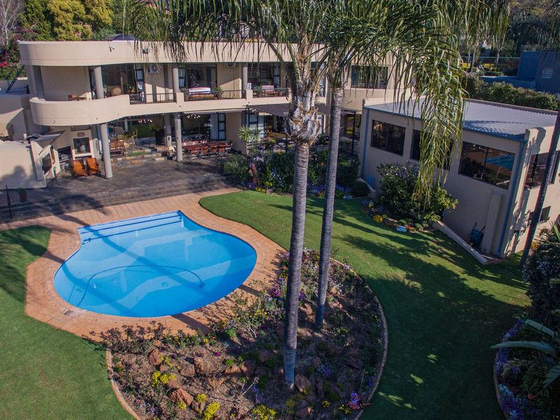 Aerial view of a spacious property featuring a large swimming pool, manicured garden, paved patio area, and a multi-level residence with balconies.