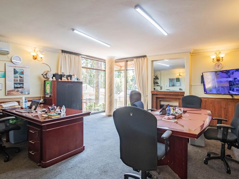 A spacious home office featuring built-in fireplace, decorative crown molding, wall paneling, and large sliding glass doors providing natural light and garden access.
