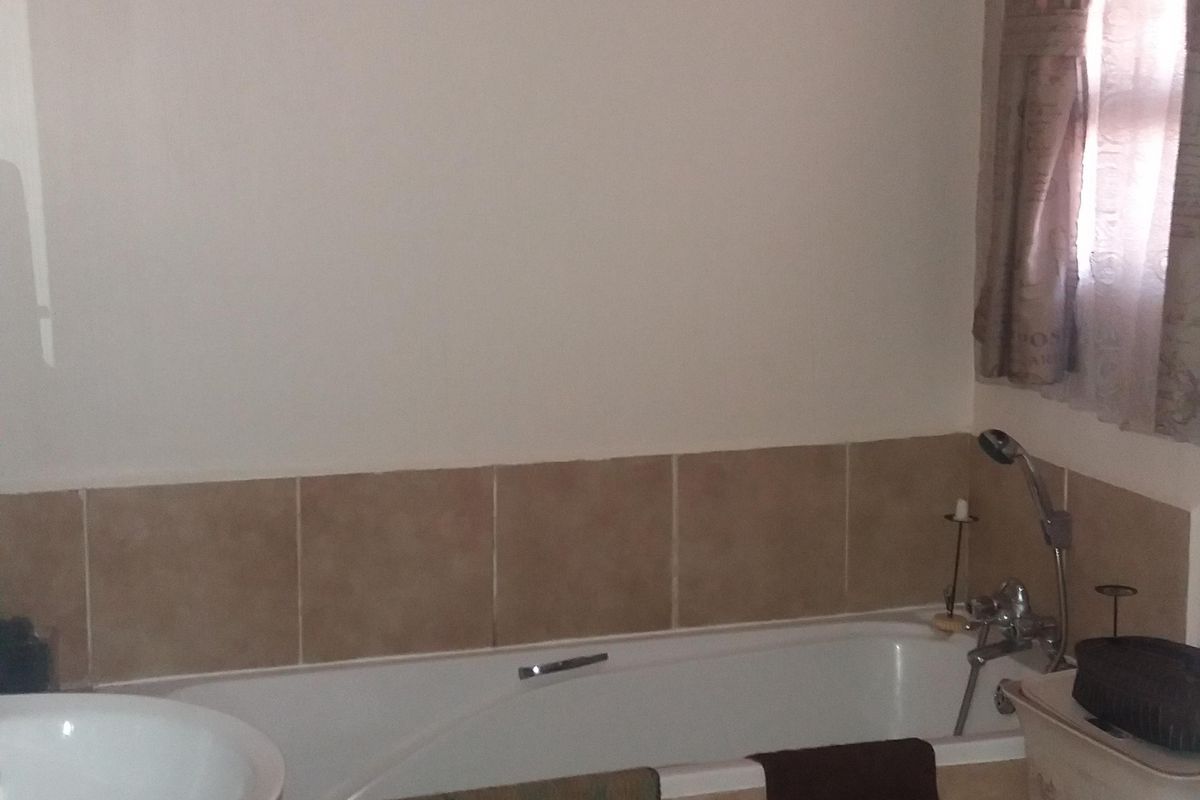 A functional bathroom featuring a pedestal basin, a built-in bathtub with tiled surround, and neutral ceramic floor tiling.