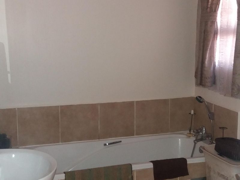 A functional bathroom featuring a pedestal basin, a built-in bathtub with tiled surround, and neutral ceramic floor tiling.