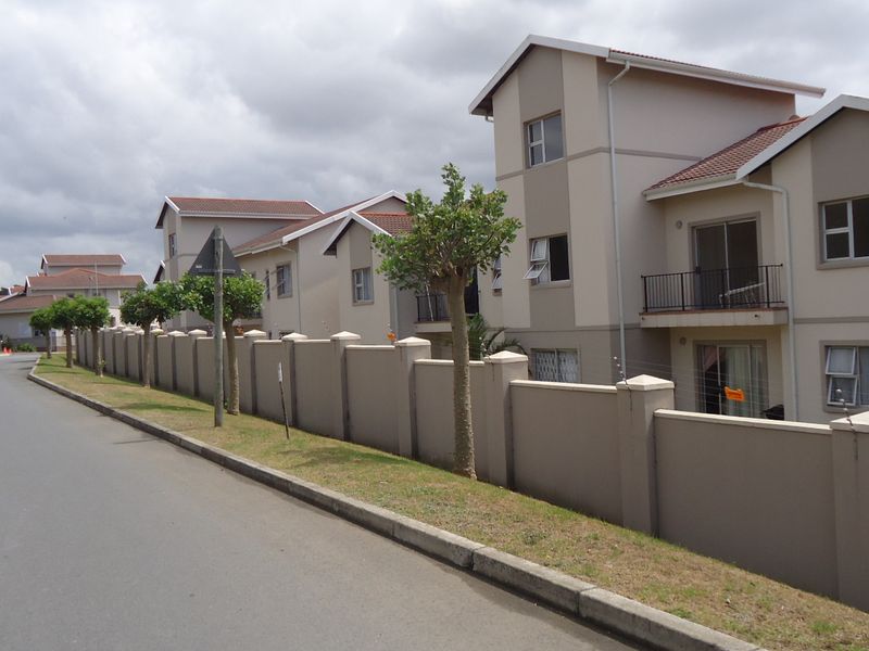 Exterior view of a multi-unit apartment complex featuring perimeter walling, electric fencing, and balconies, situated along a paved street.