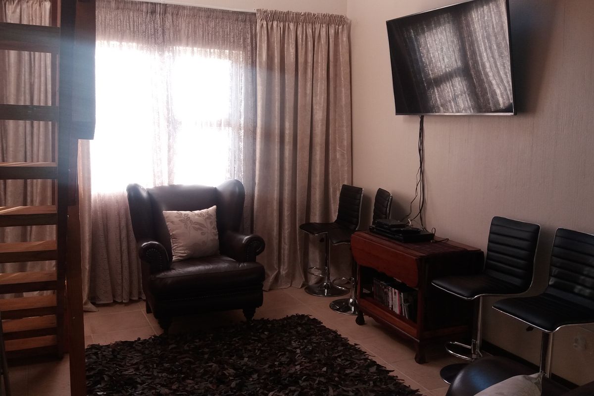 A living area featuring tiled flooring, window treatments, and a wall-mounted television setup, providing a functional space for relaxation.