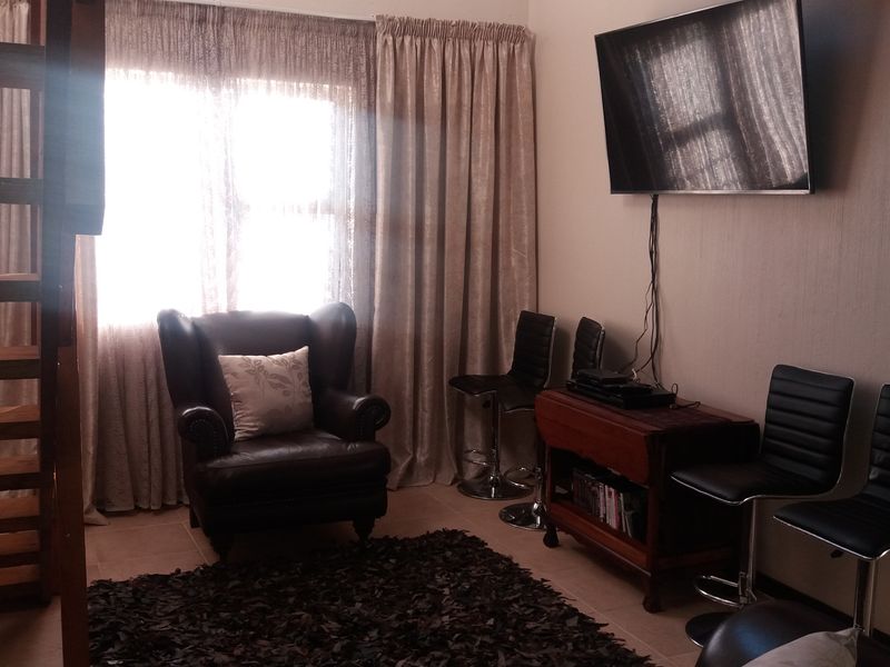 A living area featuring tiled flooring, window treatments, and a wall-mounted television setup, providing a functional space for relaxation.