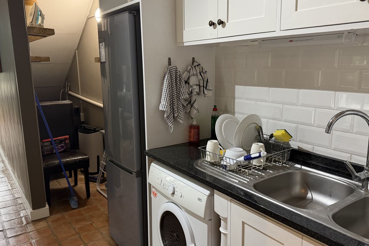 Compact kitchen area featuring white cabinetry, subway tile backsplash, dark countertops, and an integrated washing machine, with adjacent utility space under the stairs.