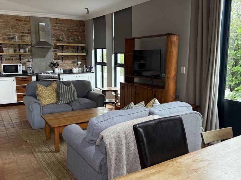 Spacious open-plan living area featuring an exposed brick kitchen wall, terracotta flooring, and direct access to the garden through French doors.