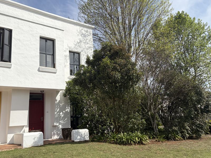 Front elevation of a white townhouse featuring a red timber entrance door, sash windows, and a landscaped garden area with built-in masonry seating.
