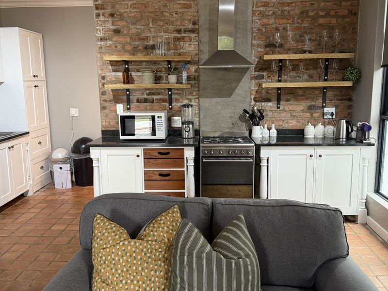 Open-plan kitchen featuring white cabinetry, exposed brick feature wall, gas stove, and terracotta flooring, seamlessly integrated with the living area.