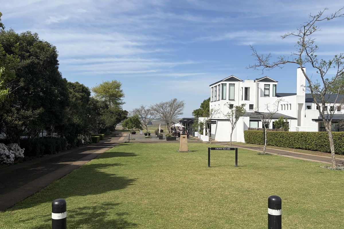 A well-maintained communal garden area featuring manicured lawns, paved walkways, and mature hedging, set against a modern white townhouse exterior.