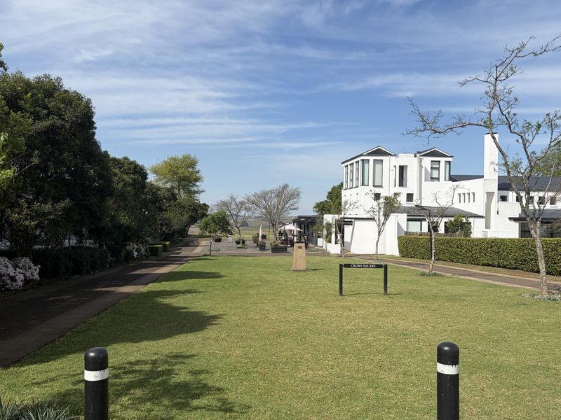 A well-maintained communal garden area featuring manicured lawns, paved walkways, and mature hedging, set against a modern white townhouse exterior.