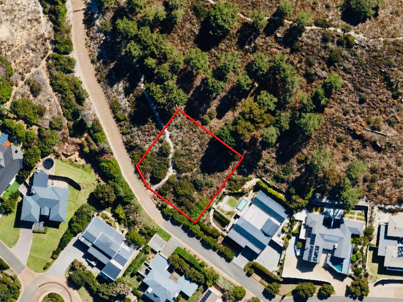 Aerial view of a vacant residential plot situated in a developed neighborhood, featuring natural vegetation and sloped topography.