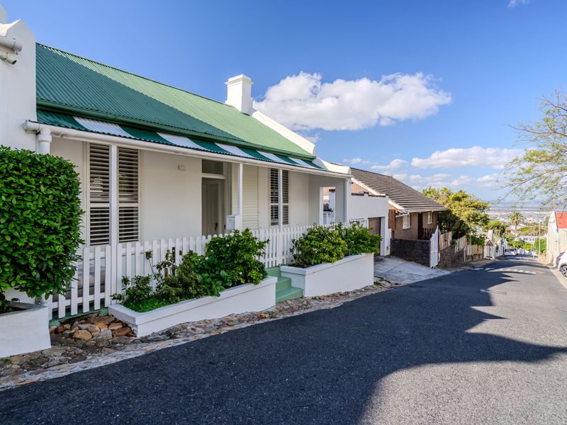 Charming cottage-style home featuring a green corrugated metal roof, white picket fencing, and built-in planter boxes along the street-facing facade.