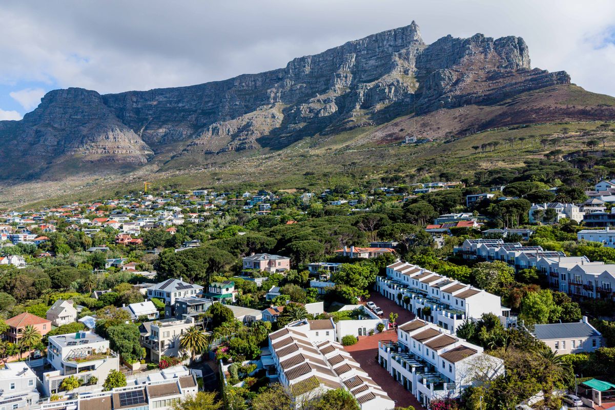 An elevated aerial view of a residential neighborhood nestled at the base of a prominent mountain range, showcasing the surrounding landscape and housing density.
