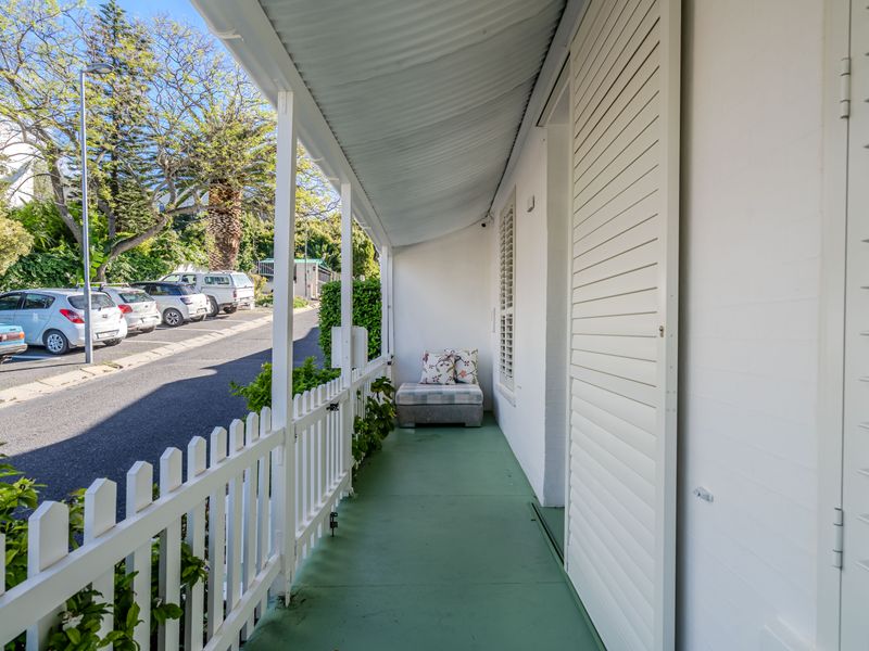 A covered front veranda featuring a painted concrete floor, white picket fencing, and louvered shutters, providing a charming entrance to the home.