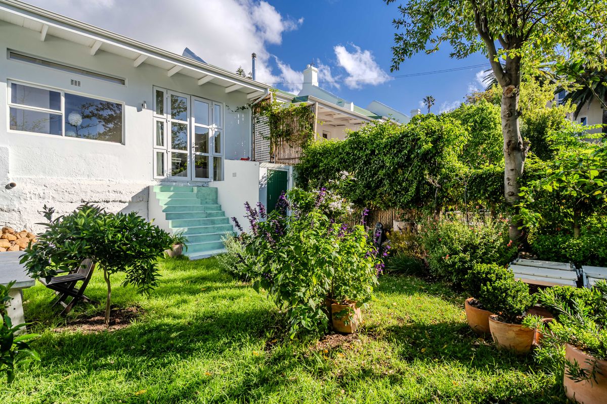 Rear view of the property featuring a landscaped garden, concrete stairs leading to french doors, and exposed roof rafters.