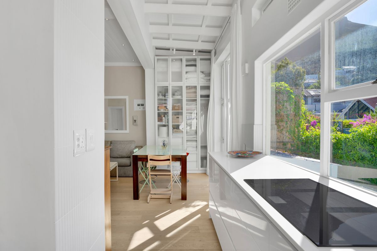 Modern kitchen featuring sleek white cabinetry, a built-in hob, and a coffered ceiling, with large windows providing ample natural light and garden views.