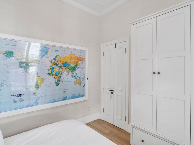 A well-maintained bedroom featuring light timber flooring, coving, and a built-in wardrobe with classic panel detailing.