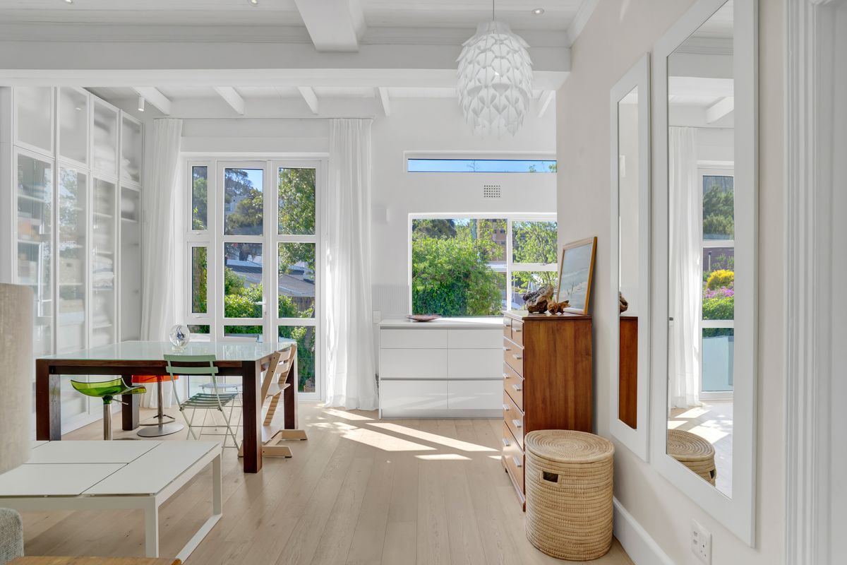 Bright and airy living space featuring timber flooring, exposed ceiling beams, and extensive built-in cabinetry with large windows providing natural light and garden views.