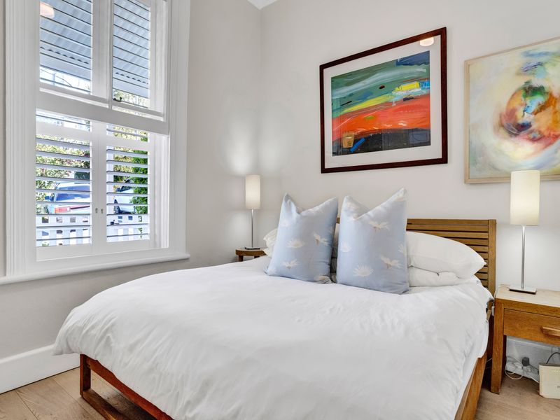 A well-maintained bedroom featuring timber flooring and white plantation shutters, offering a bright and clean aesthetic.
