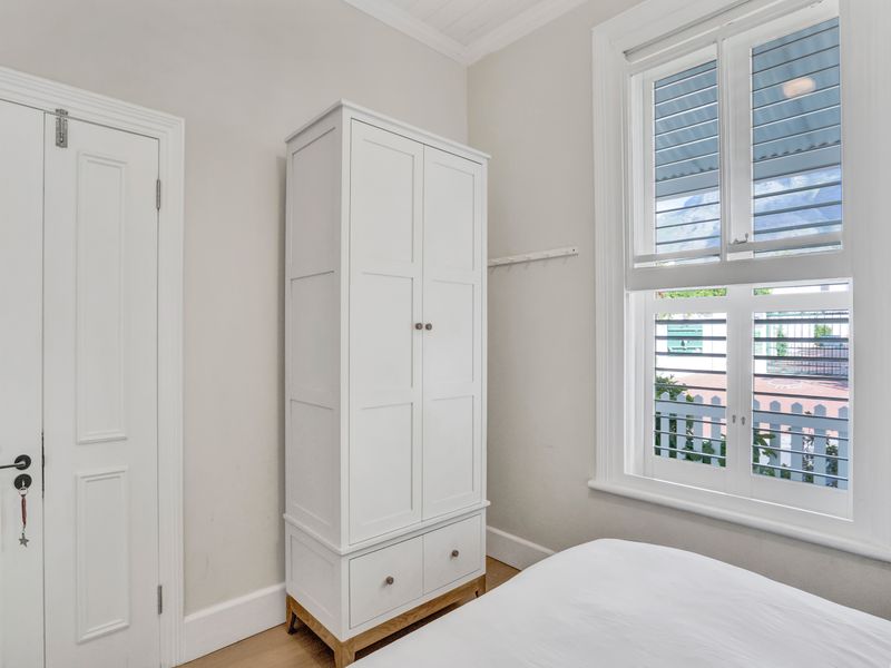 A bright bedroom featuring timber flooring, classic panelled doors, and white timber window shutters, offering a clean and well-maintained living space.