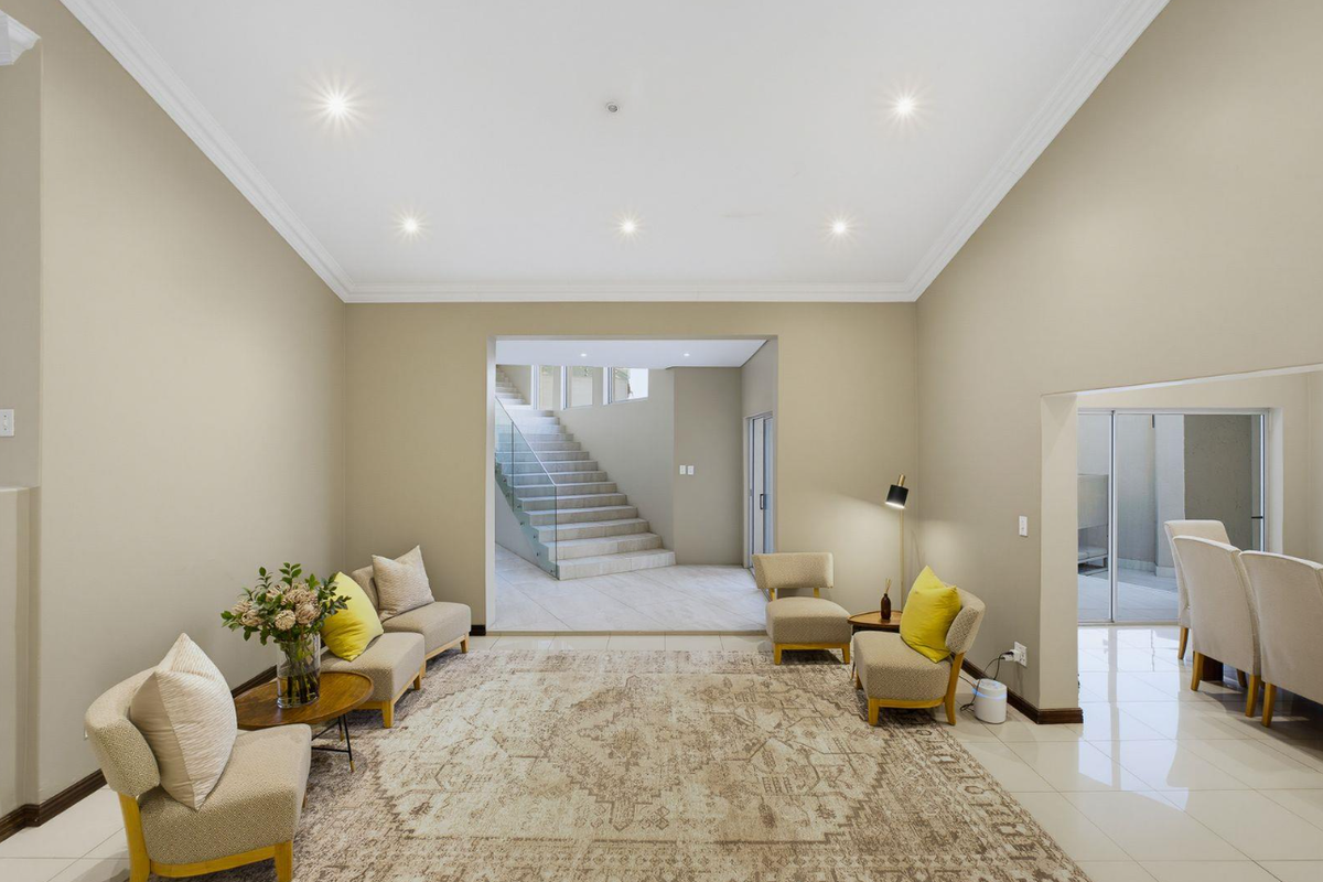 Spacious living area featuring neutral walls, recessed downlighting, crown molding, and polished tile flooring, with an open transition to a modern staircase.
