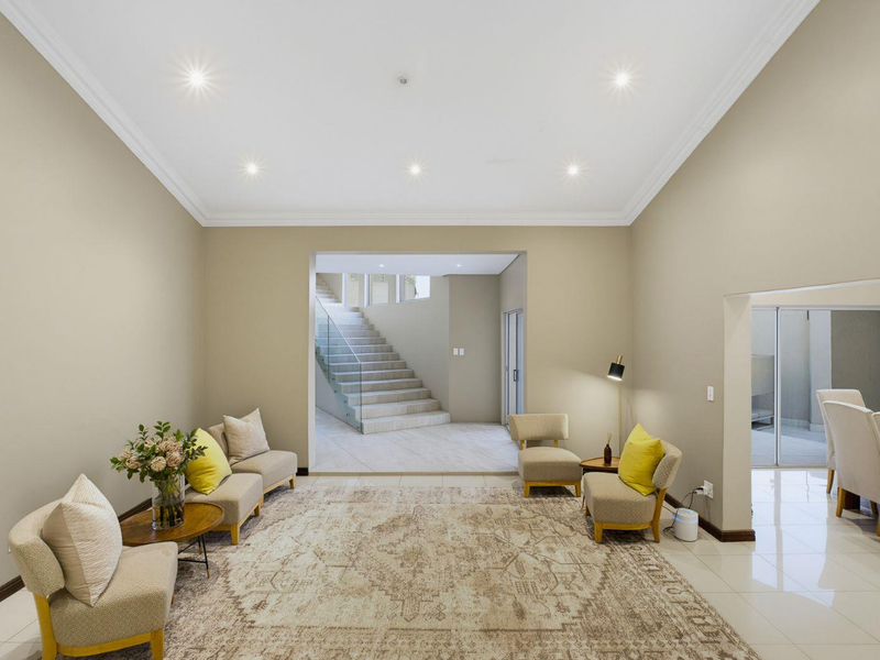 Spacious living area featuring neutral walls, recessed downlighting, crown molding, and polished tile flooring, with an open transition to a modern staircase.