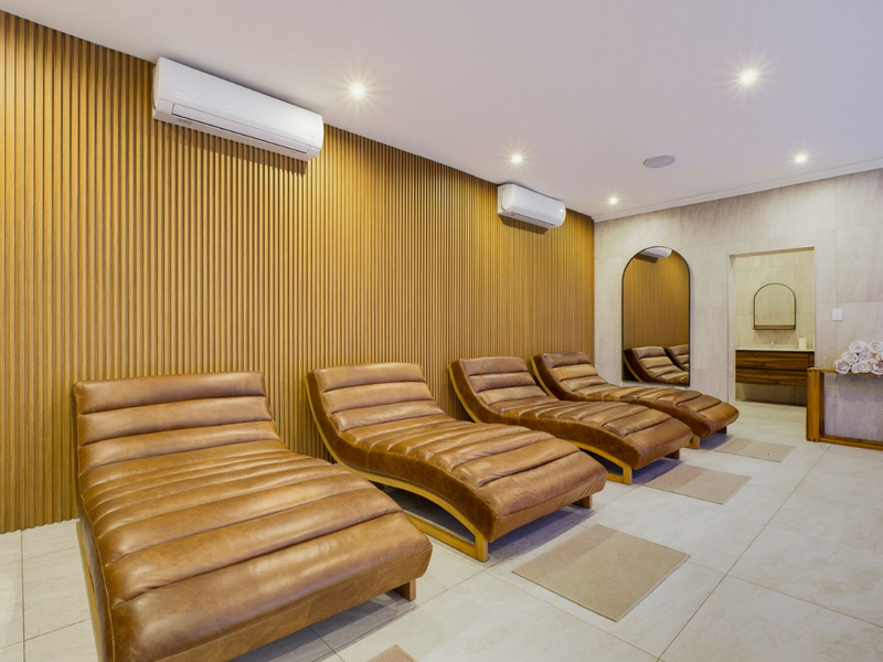 A modern relaxation room featuring slatted timber wall paneling, tiled flooring, recessed lighting, and dual split-system air conditioning units.