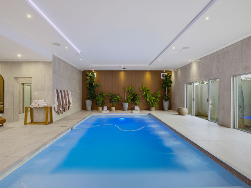 A luxurious indoor swimming pool area featuring a wood slat accent wall, recessed lighting, and large sliding glass doors opening to the exterior.