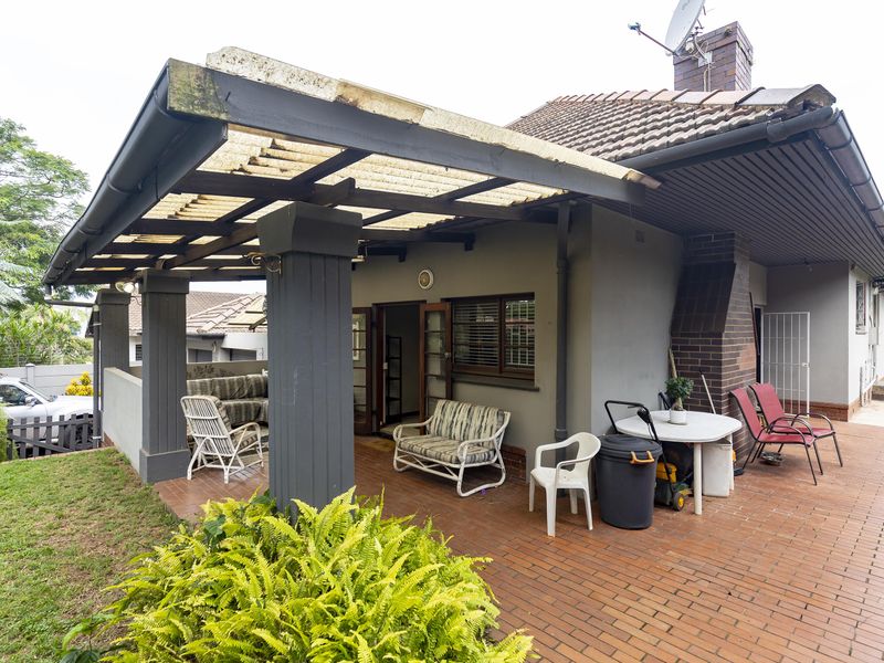 A covered outdoor patio area featuring brick paving, a brick chimney, and structural support columns, providing a functional space for outdoor living.