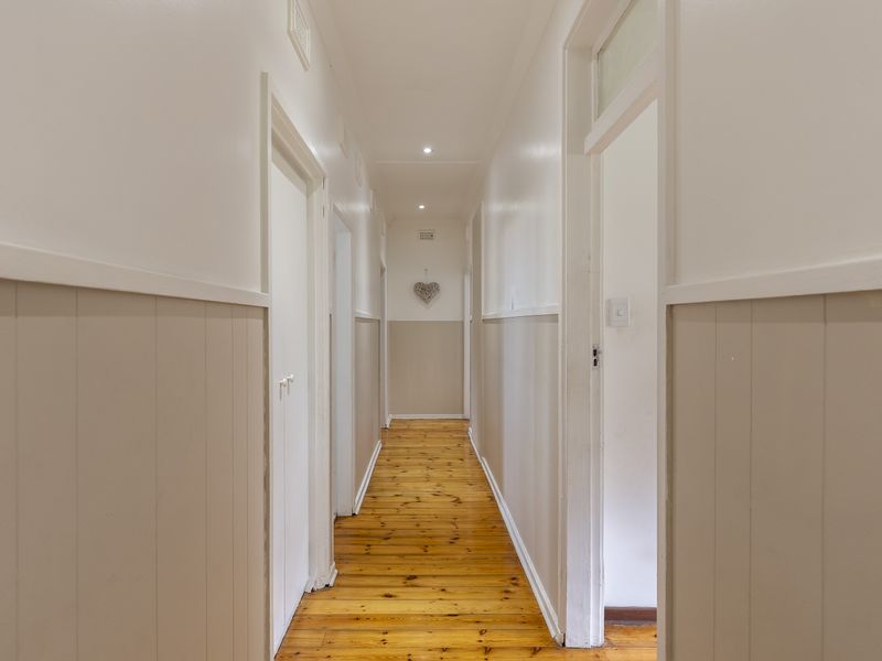 A bright, well-maintained hallway featuring polished timber flooring and classic wainscoting, providing a clean and inviting transition between rooms.