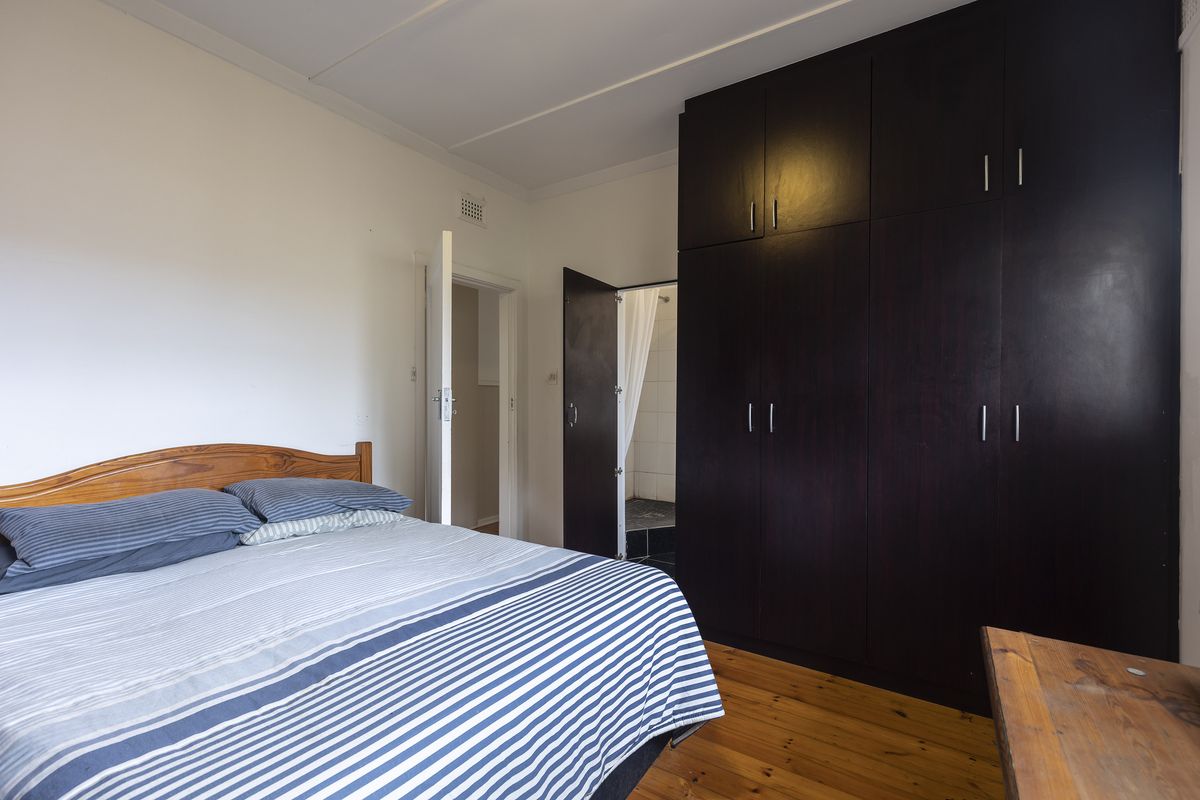 A bedroom featuring dark wood built-in cupboards, polished hardwood flooring, and direct access to an en-suite bathroom.