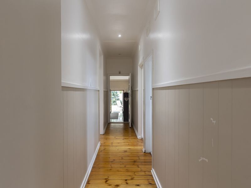 A bright hallway featuring polished timber flooring and neutral wainscoting, providing a clean transition between rooms.